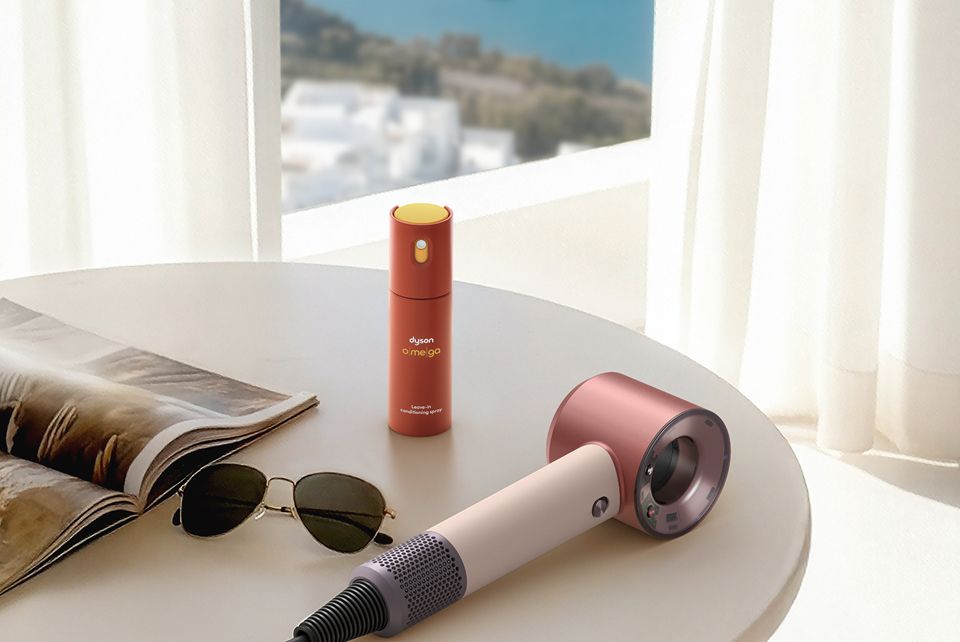 Dyson Supersonic Travel hair dryer on a table with Dyson Omega leave-in conditioning spray.