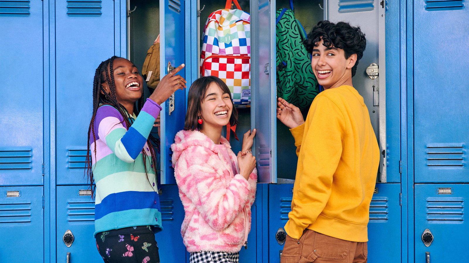 Three teenagers smiling with blue lockers in the background