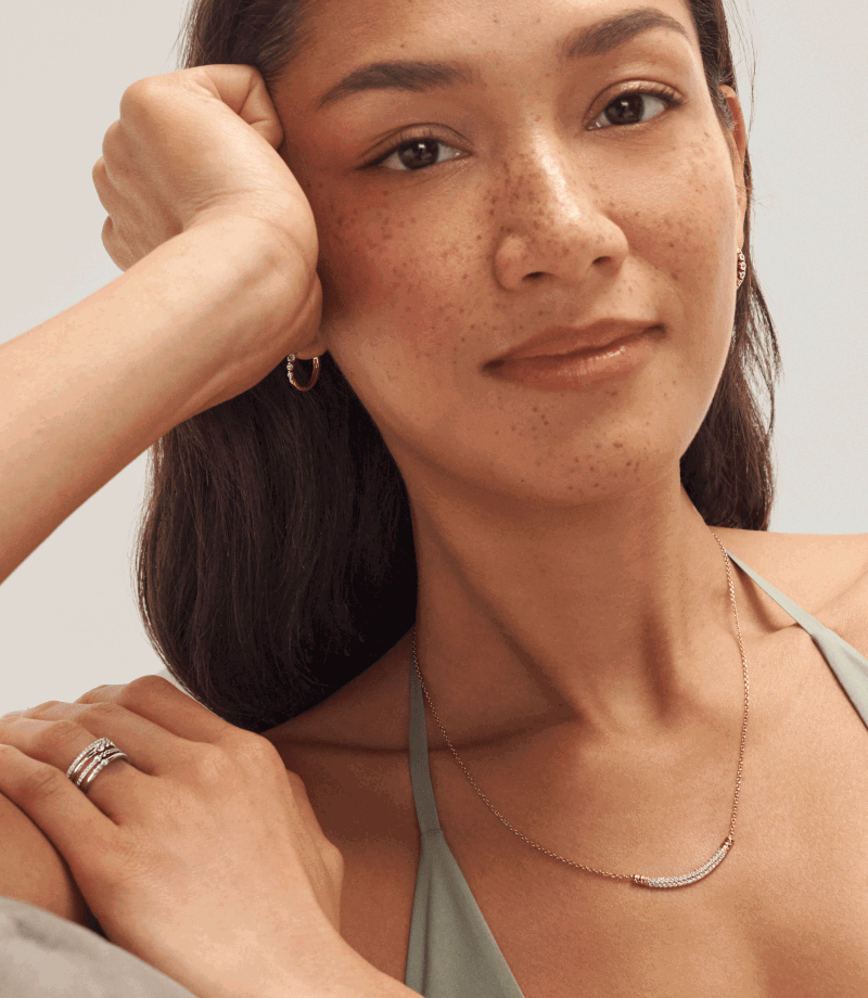 Female model wearing a curved diamond pendant necklace, rings and hoops.