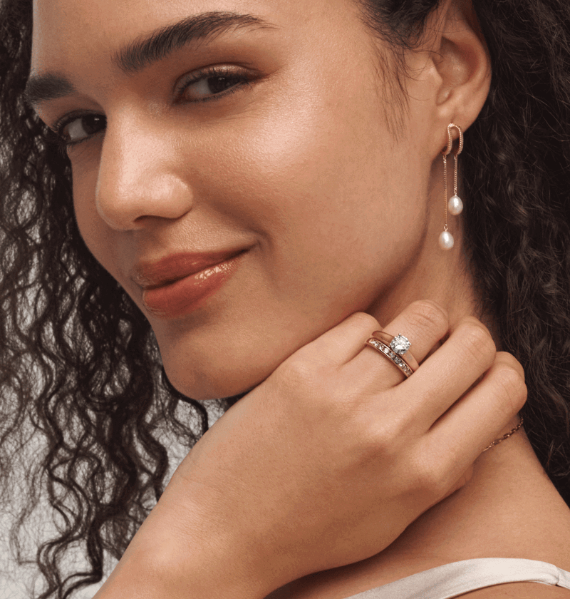 Close-up of woman wearing yellow gold pearl drop earrings and diamond bridal rings.