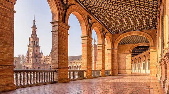 Blick durch die Backsteinbögen der Plaza de España in Sevilla auf den markanten Turm.