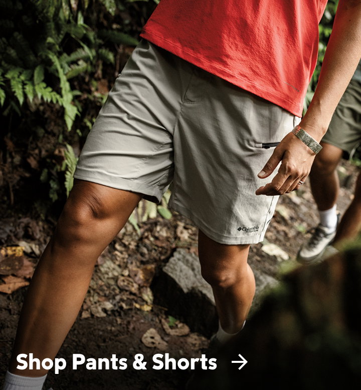 Two people hiking in a forest with text: Shop Pants & Shorts 