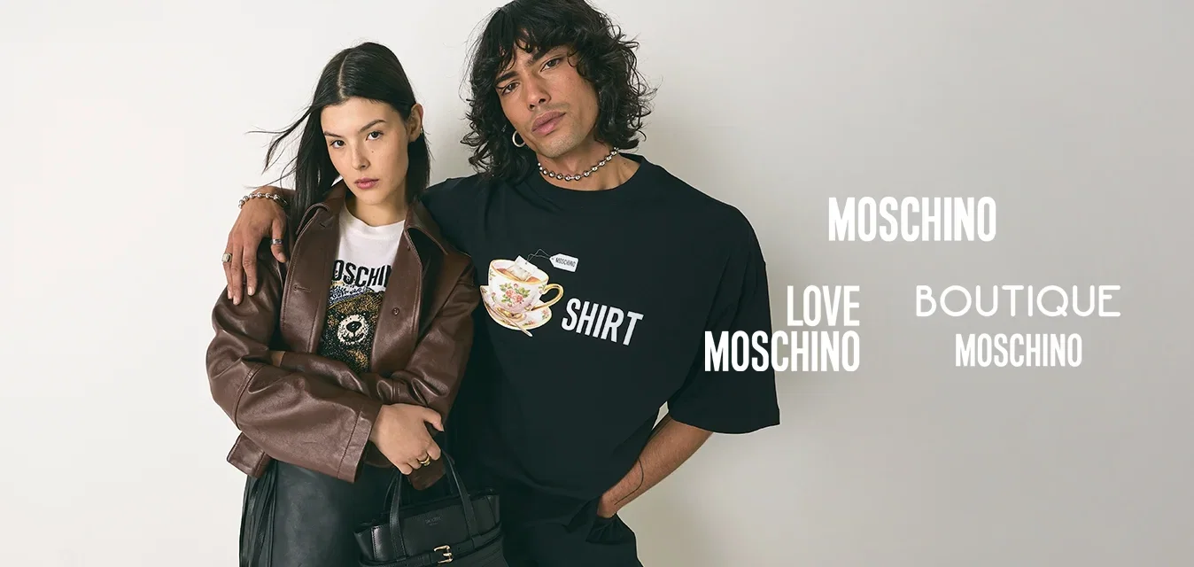 Jeune homme aux cheveux bouclés portant un t-shirt noir avec un motif graphique, avec le bras autour d'une femme vêtue d'une veste marron, d'une jupe noire et tenant un sac à main noir.