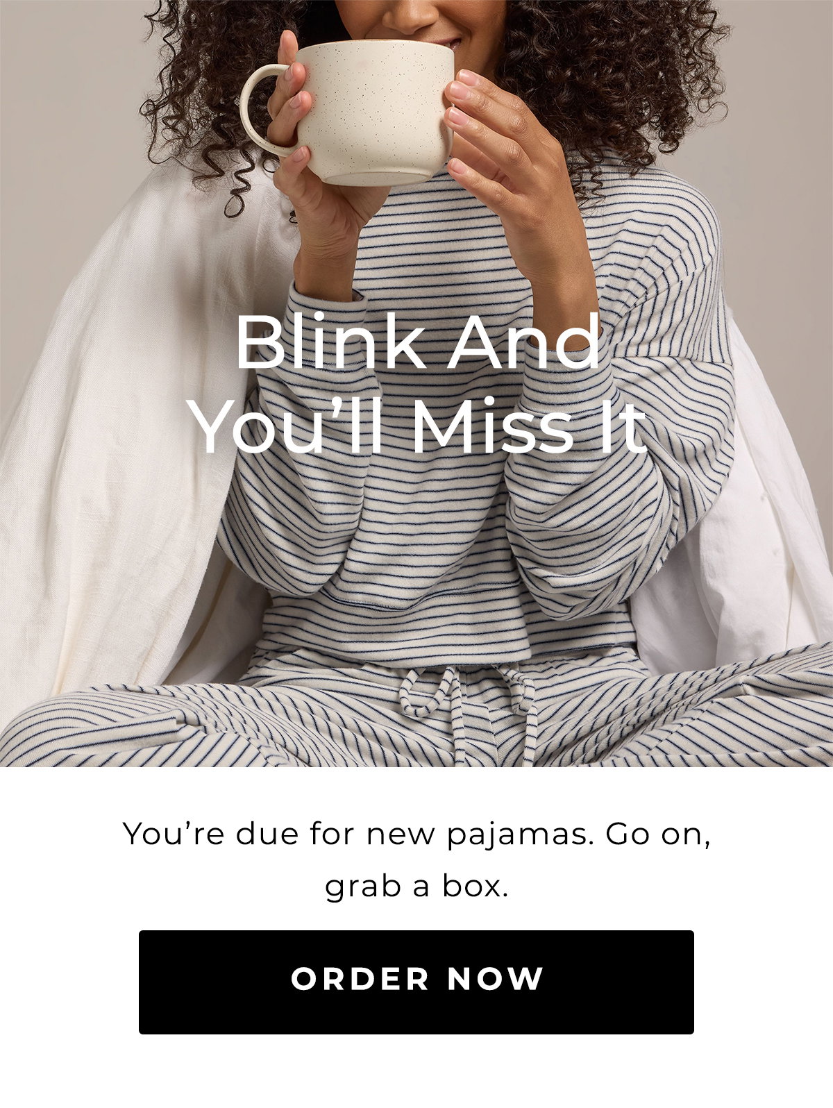 Woman in blue striped pajamas sipping from a mug while seated beneath a white blanket.