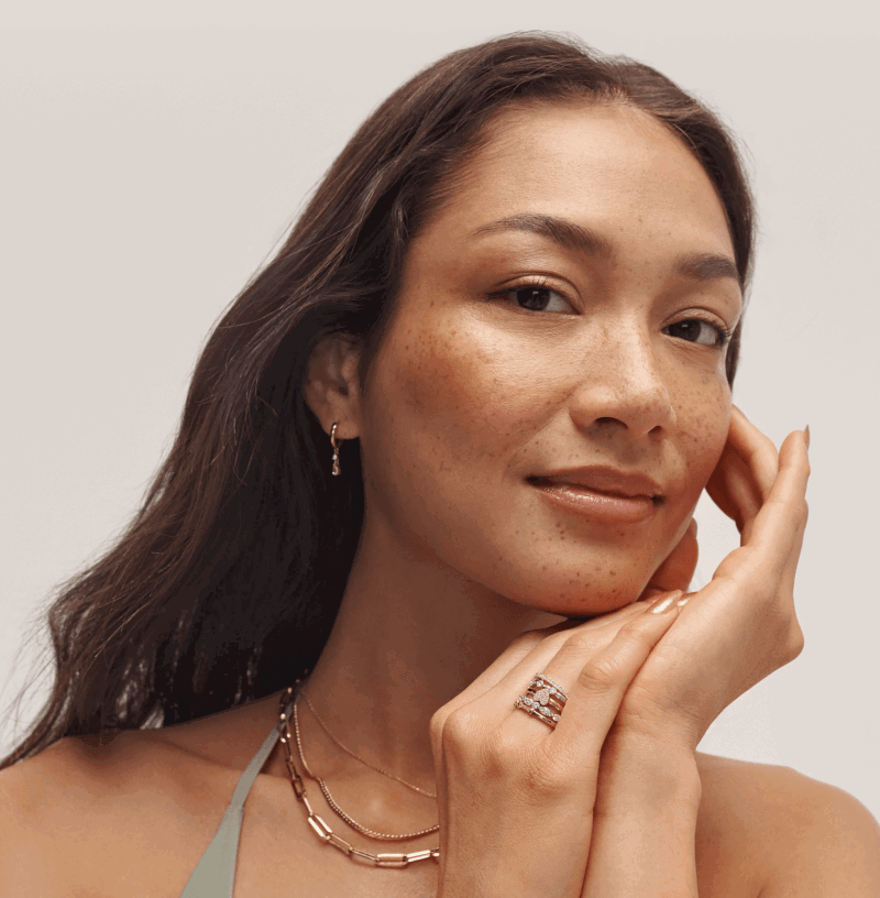 Woman wearing layered gold necklaces, a gold bracelet, stacked rings, and gold drop earrings.