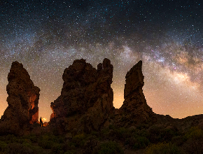 Silhouetted rock formations under a starry night sky with the Milky Way visible.