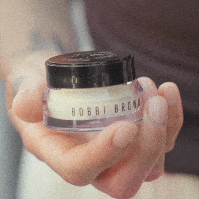Hand holding an open jar of the new Vitamin Enriched Face Base+ and scooping the cream with a finger.