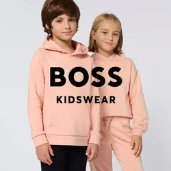 Dos niños de pie uno al lado del otro con sudaderas con capucha de color melocotón, uno con el texto 