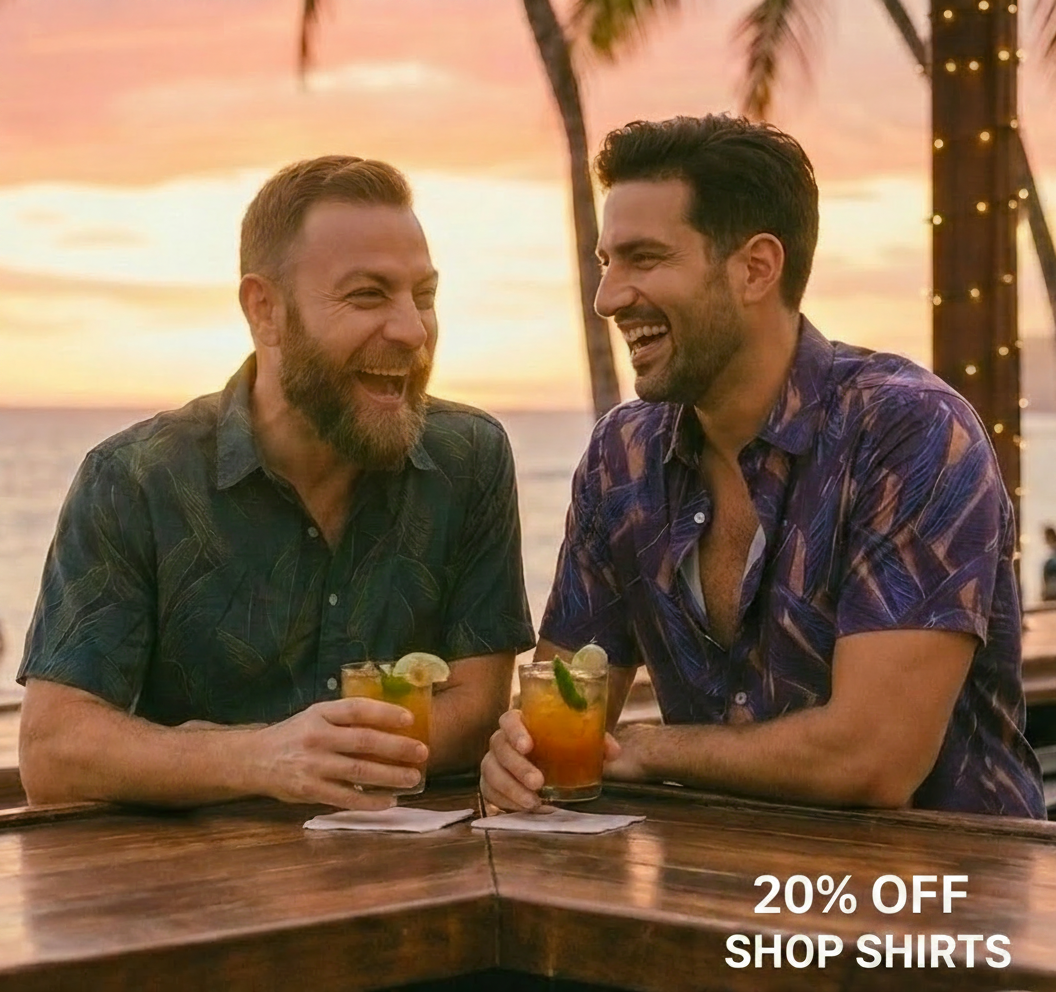 Two men laugh while holding drinks at a bar with a beach sunset in the background.
