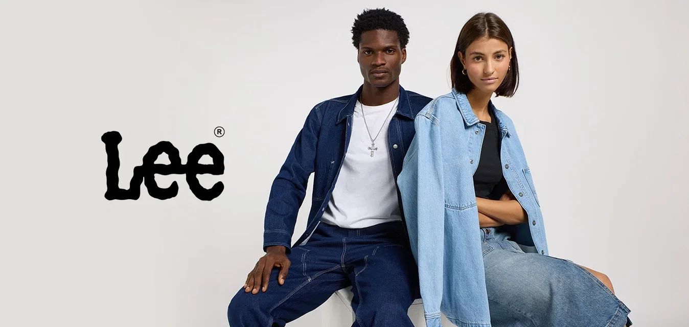 Man en vrouw zitten naast elkaar op een wit blok, beiden gekleed in denim outfits tegen een effen lichte achtergrond.