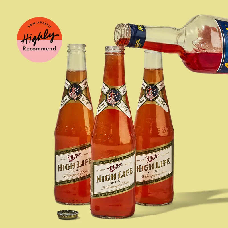 Aperol being poured into 3 bottles of Miller High Life for Spaghett cocktails.