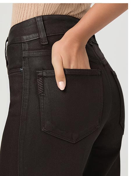 Detail shot of a woman wearing dark brown coated denim jeans.