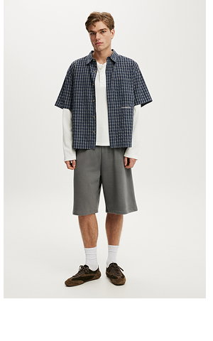 Male model wearing checked shirt, white tee, and grey shorts