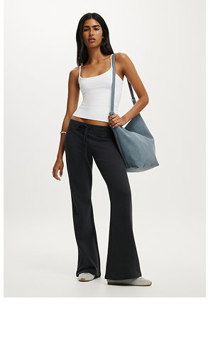 Woman wearing white tank top, black flared pants, and blue shoulder bag