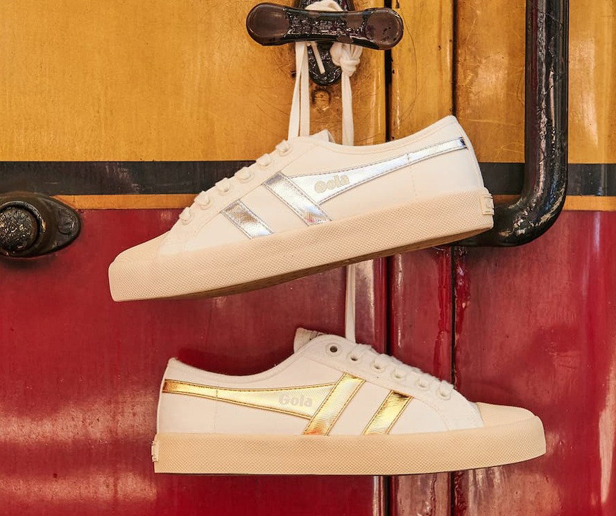 An image of Gola Coaster in white/silver and white/gold hanging with their laces from a train doo. 