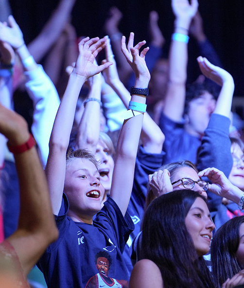 Excited fans in the stadium stands cheering with their hands raised high during a basketball game.