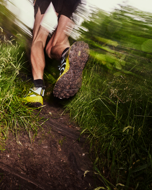 A view of the underside of a TRAILTALON MAX shoe flying through a muddy trail