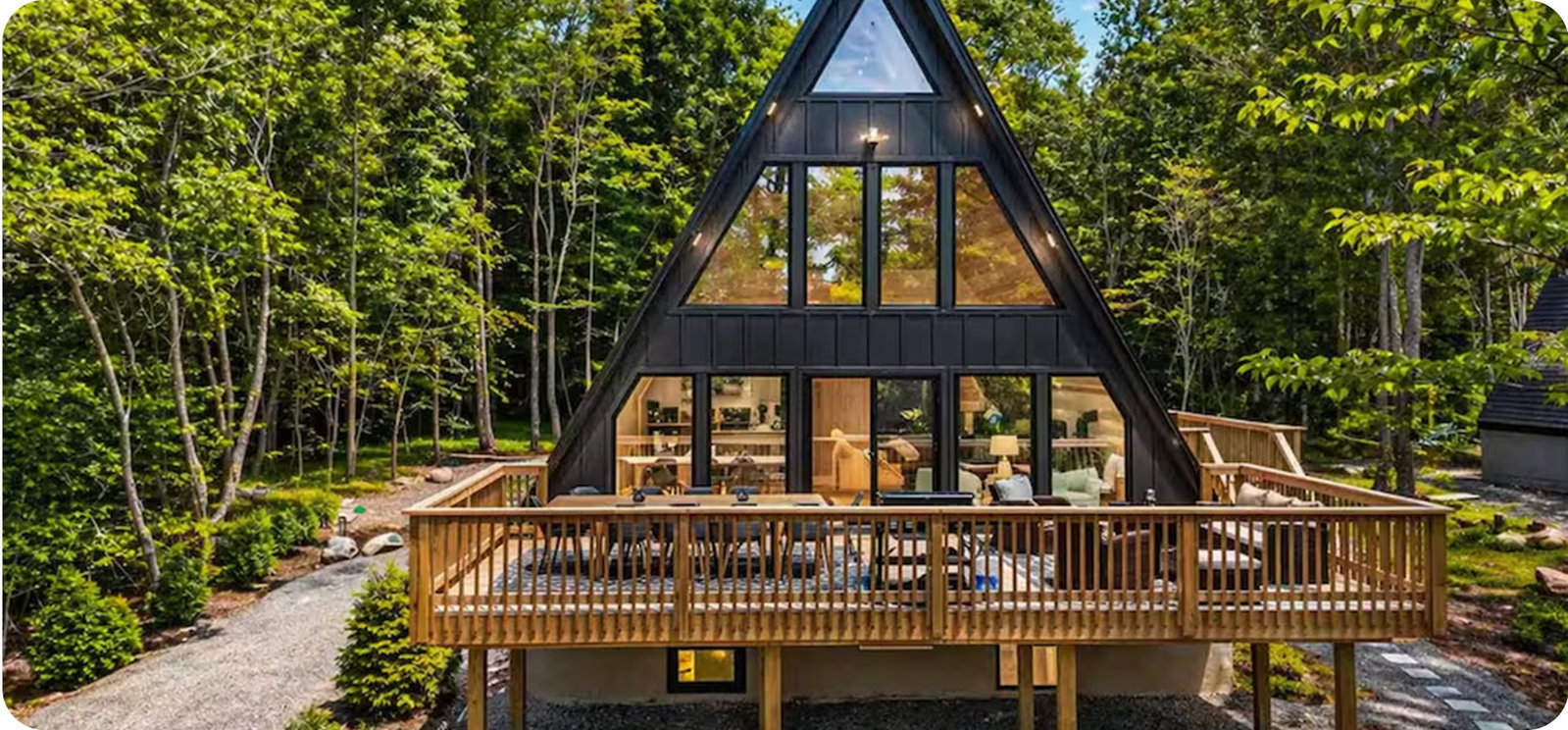 Black A-frame cabin surrounded by trees, featuring a spacious deck and large windows.