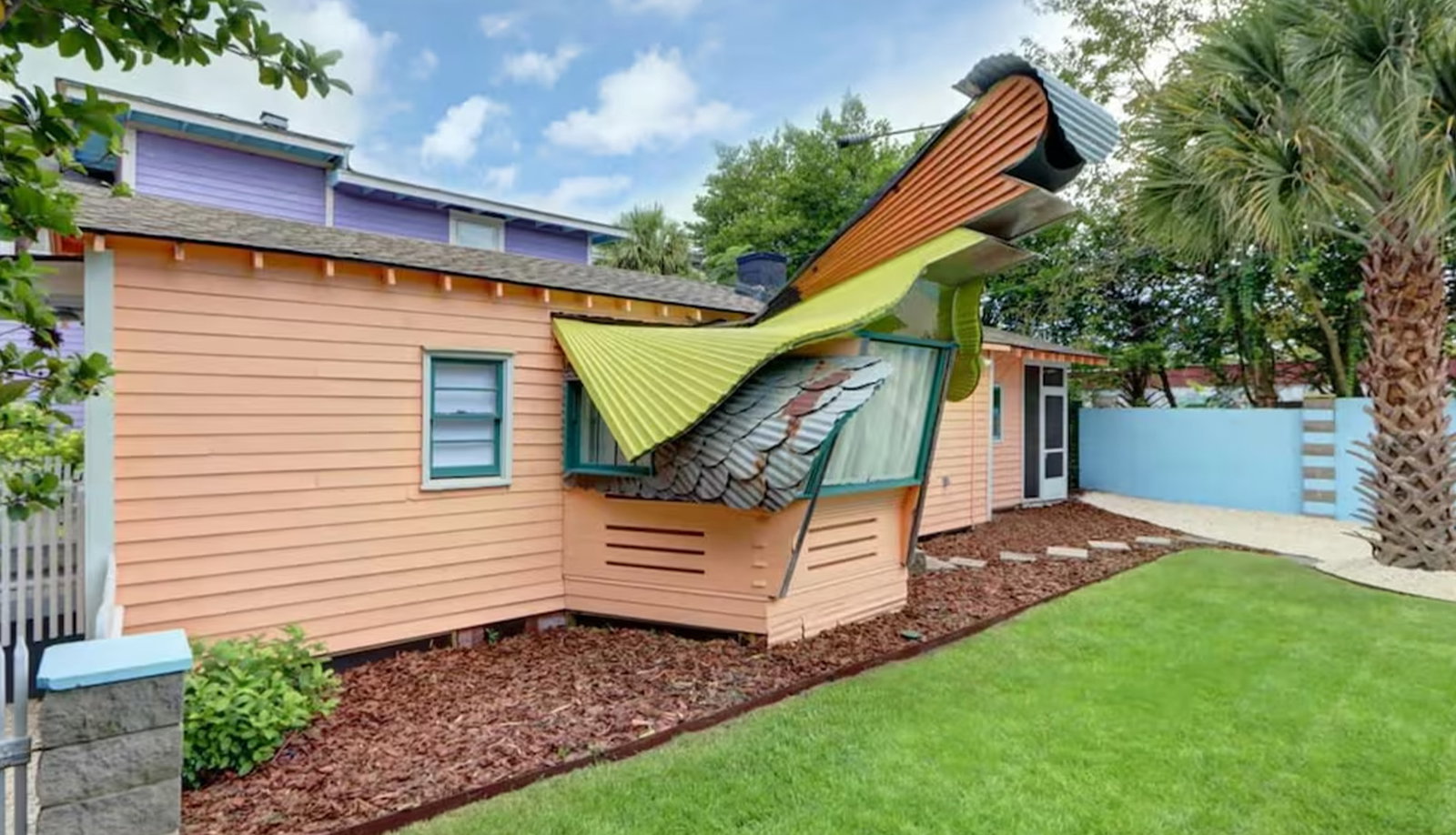 Colorful house with whimsical curved rooflines, landscaped yard, and palm trees.