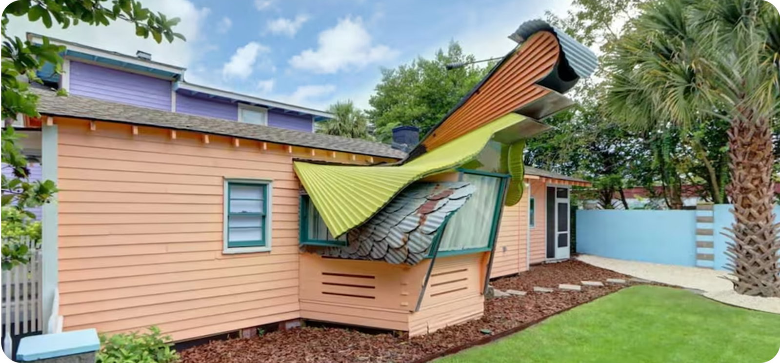 Colorful house with whimsical curved rooflines, landscaped yard, and palm trees.