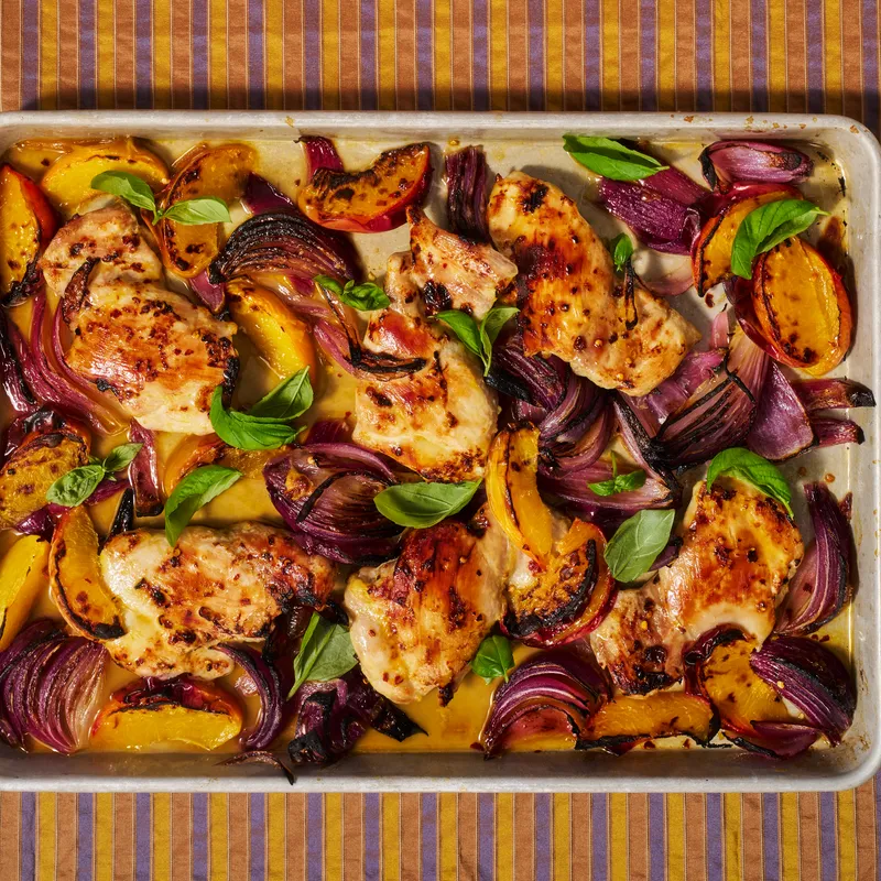 Sheet Pan Hot Honey Chicken and Peaches freshly out of the oven and place on a striped background