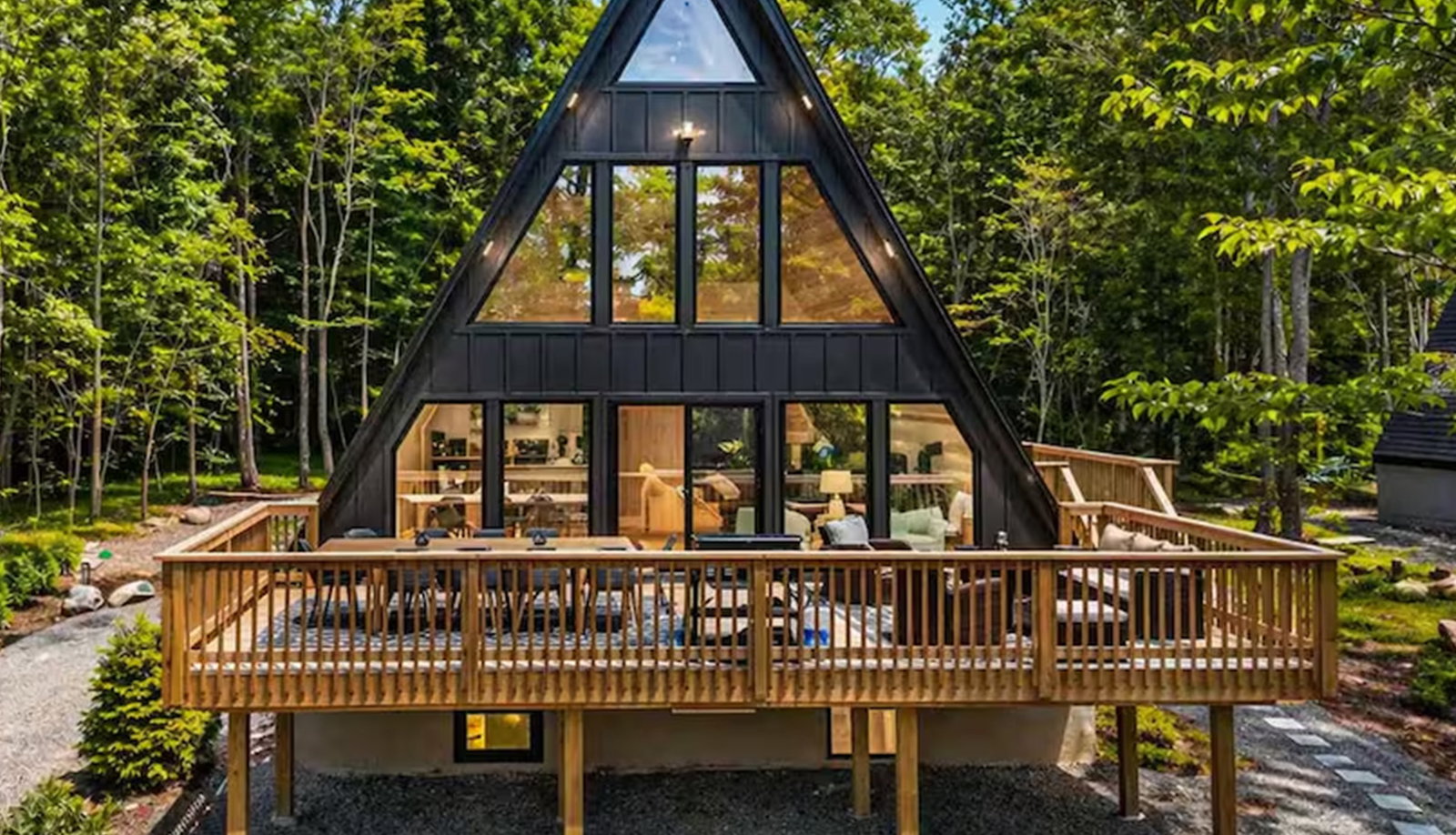 Black A-frame cabin surrounded by trees, featuring a spacious deck and large windows.
