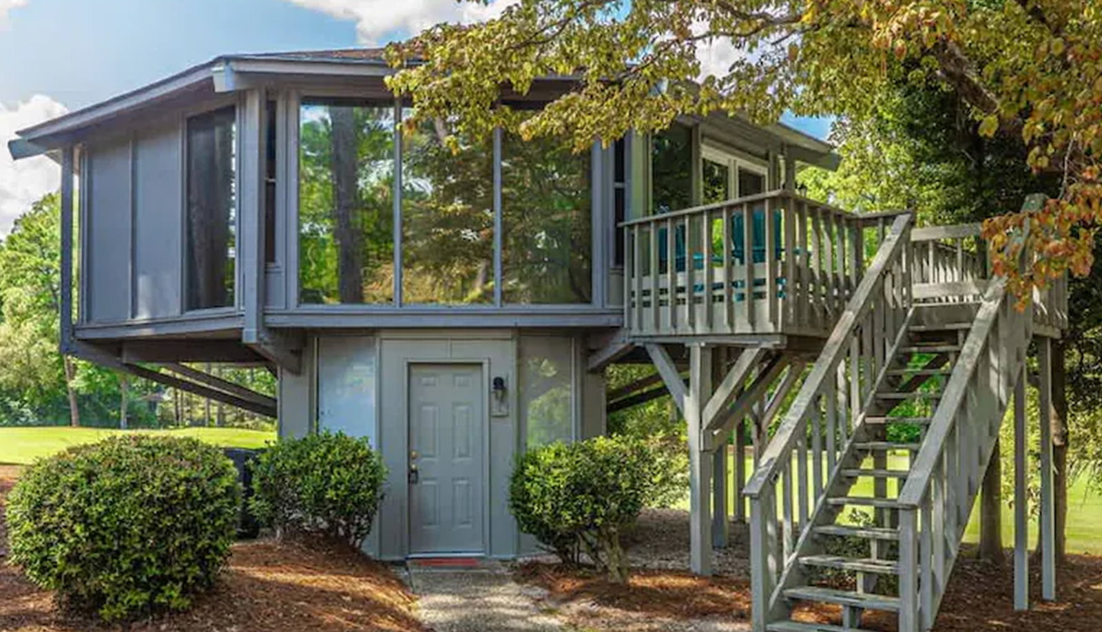 Elevated treehouse-style retreat with wraparound deck, exterior stairs, and expansive windows.