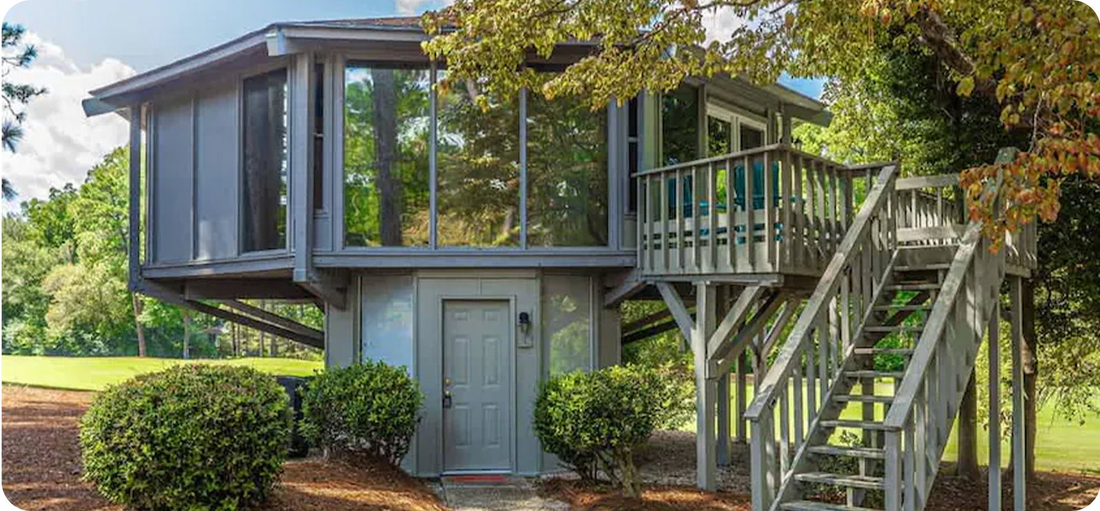 Elevated treehouse-style retreat with wraparound deck, exterior stairs, and expansive windows.