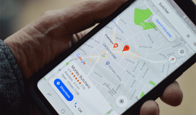 A person holds a smartphone displaying a map with a marked location named "A Meaty Butchery" with an address and options for directions and calling the place.