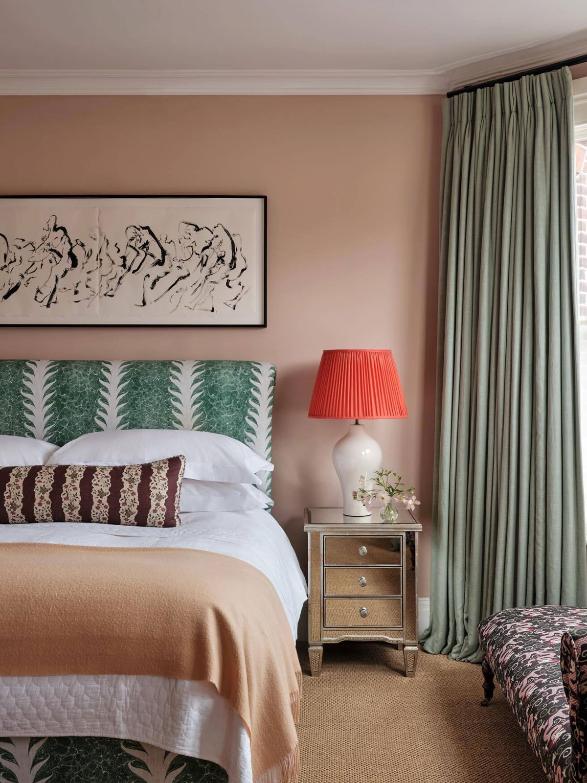 Peach walls with a green patterned headboard, red lamp, and layered bedding in soft tones.