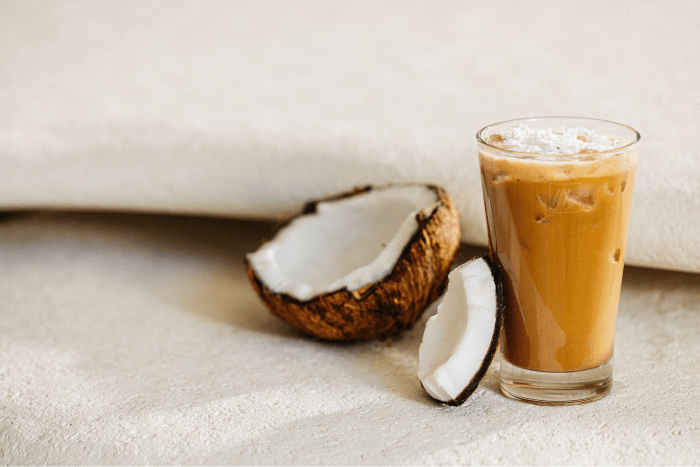 Iced coconut coffee topped with whipped cream served beside fresh coconut halves.
