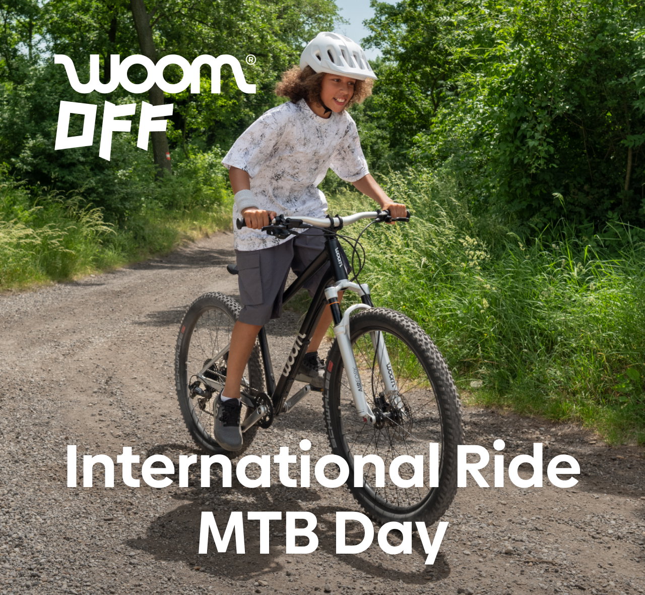 A boy rides a woom OFF AIR bike on a trail, with text overlaid reading "International Ride MTB Day"