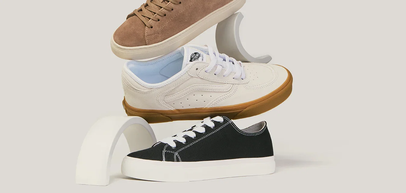 Drie casual sneakers in bruin, wit met blauwe accenten en zwart, verticaal gestapeld op witte gebogen steunen.