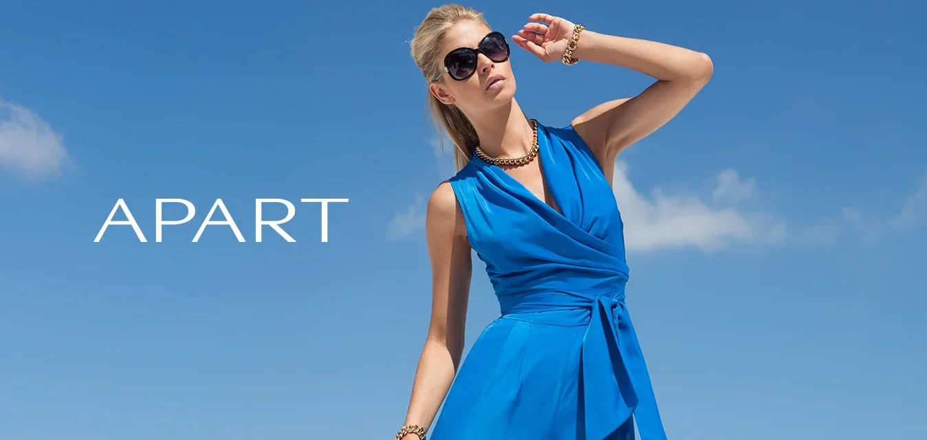 Blauwe mouwloze jumpsuit met een wikkelontwerp, striktaille en brede pijpen. Soepele textuur, gestyled met een gouden ketting en zonnebril.