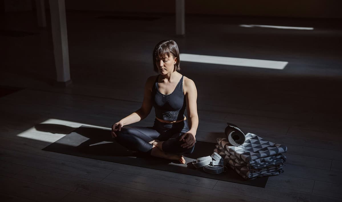 A woman sitting in a dark room on a yoga mat