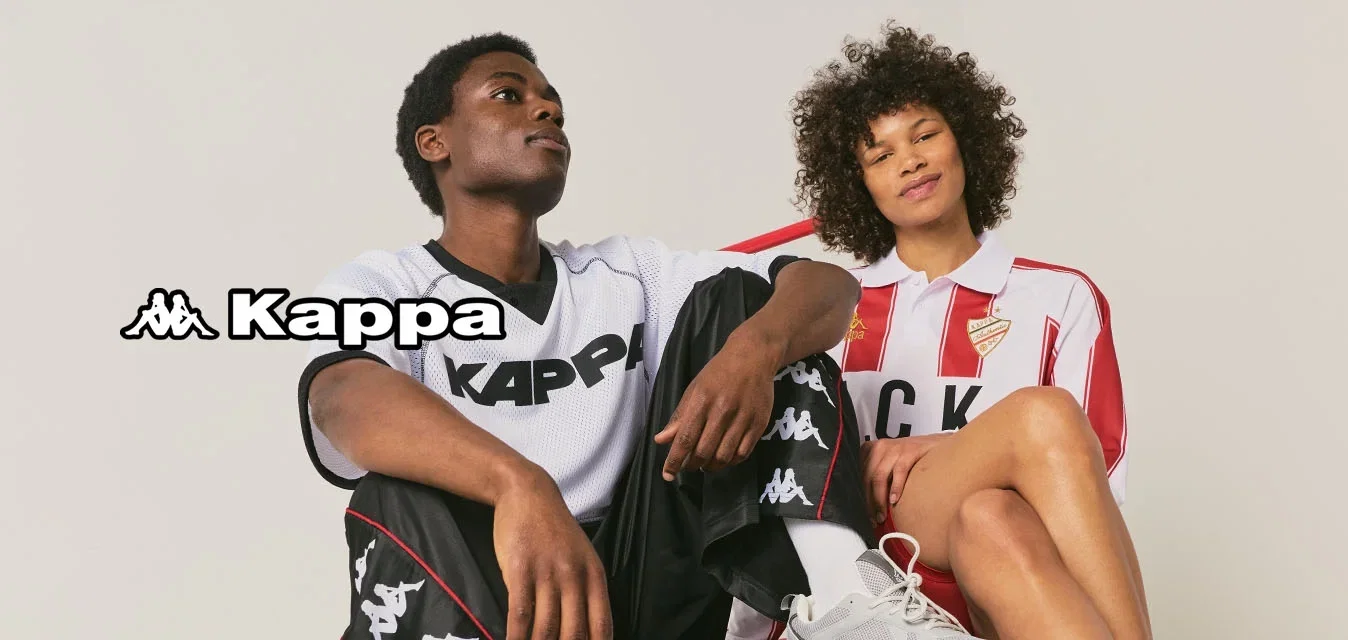 Twee mensen die Kappa sportkleding dragen zitten op een rode platformwagen tegen een effen achtergrond.