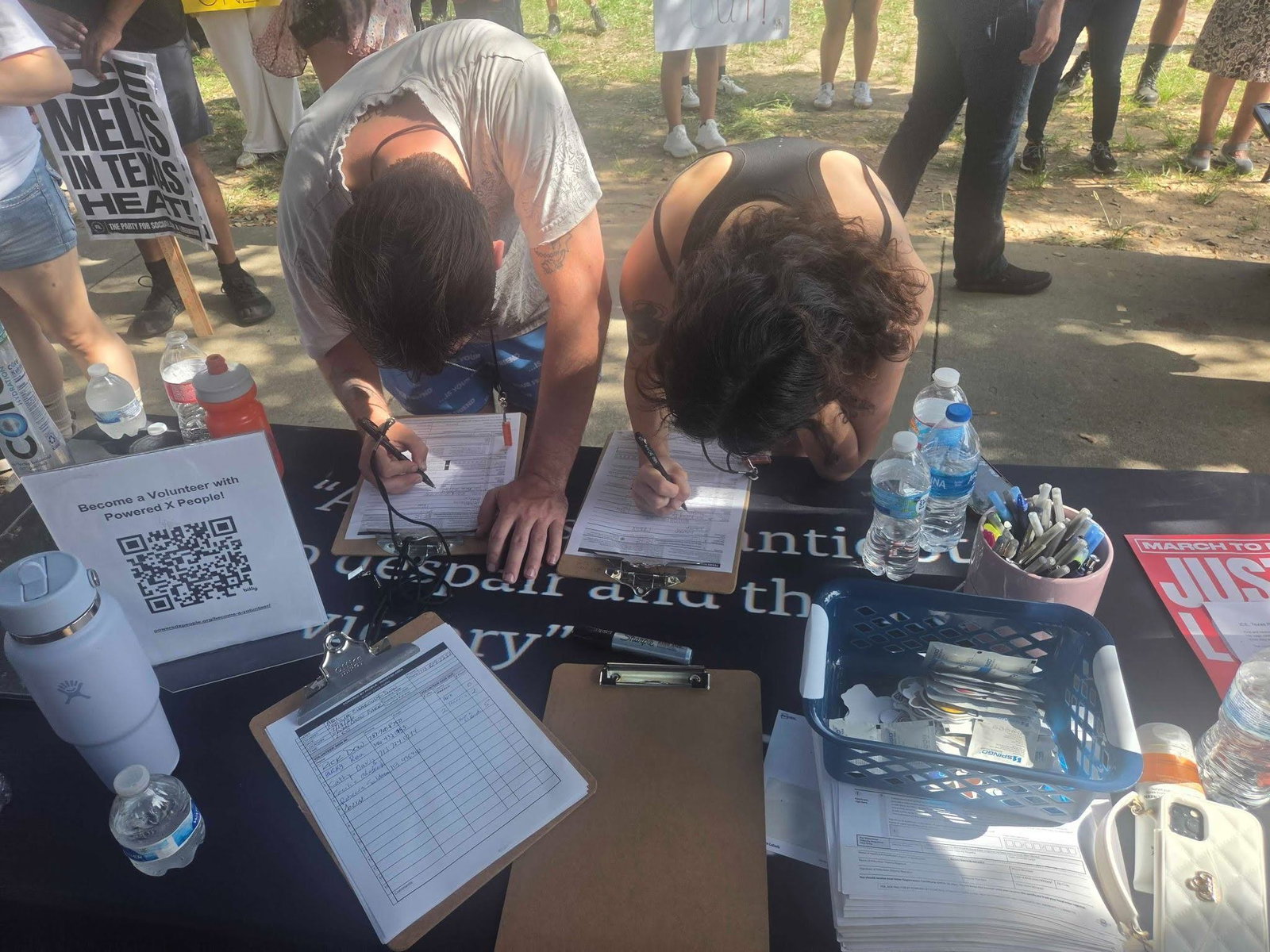 Two people filling out their voter registration forms on clipboards at a Powered by People table