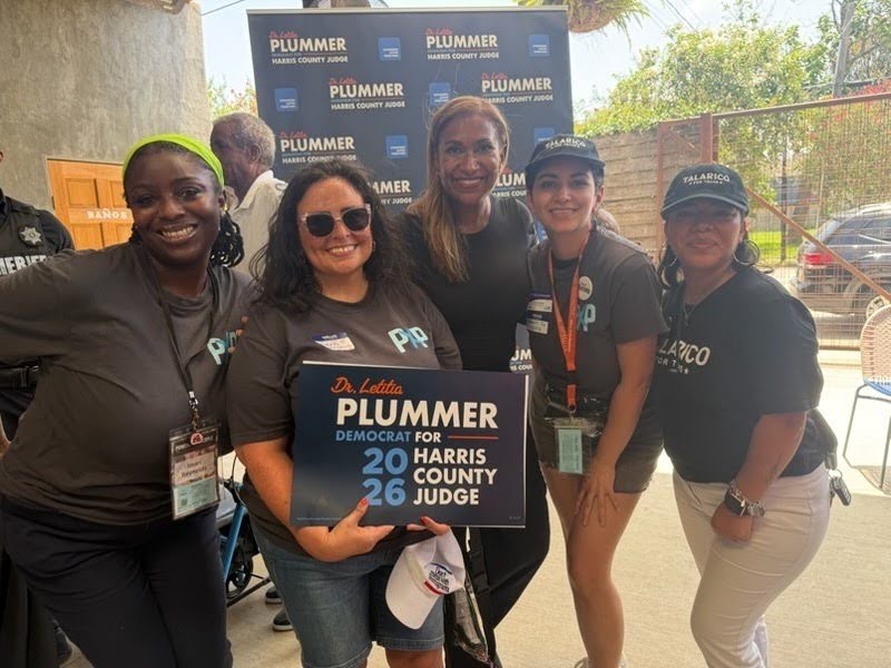 Group of Powered by People volunteers smiling at the camera standing outside. The volunteer in the center is holding a sign that says "Dr. Letitia Plummer Democrat for 2026 Harris County Judge" 