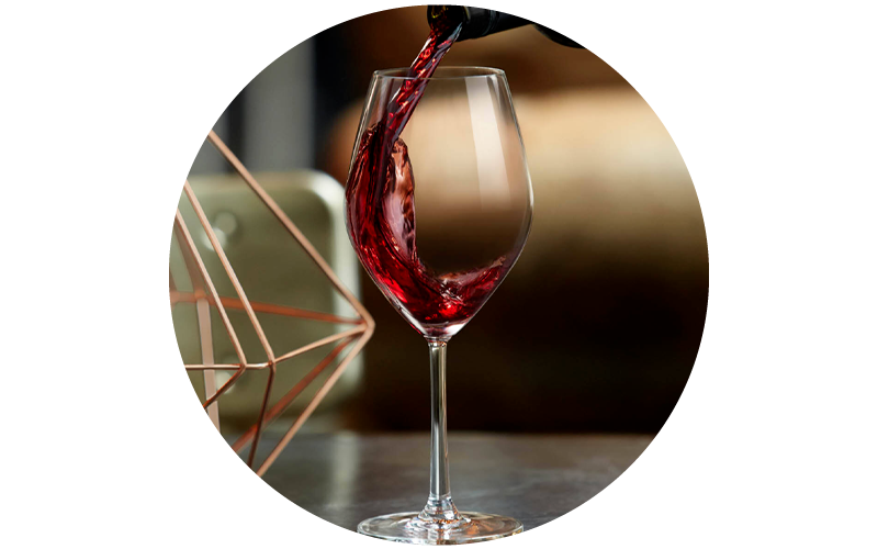 Pouring red wine into a crystal wine glass on a table, copper geometric décor and warm blurred background