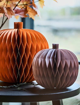A set of 2 decorative paper pumpkins in a muted orange and pink sitting atop a side table.