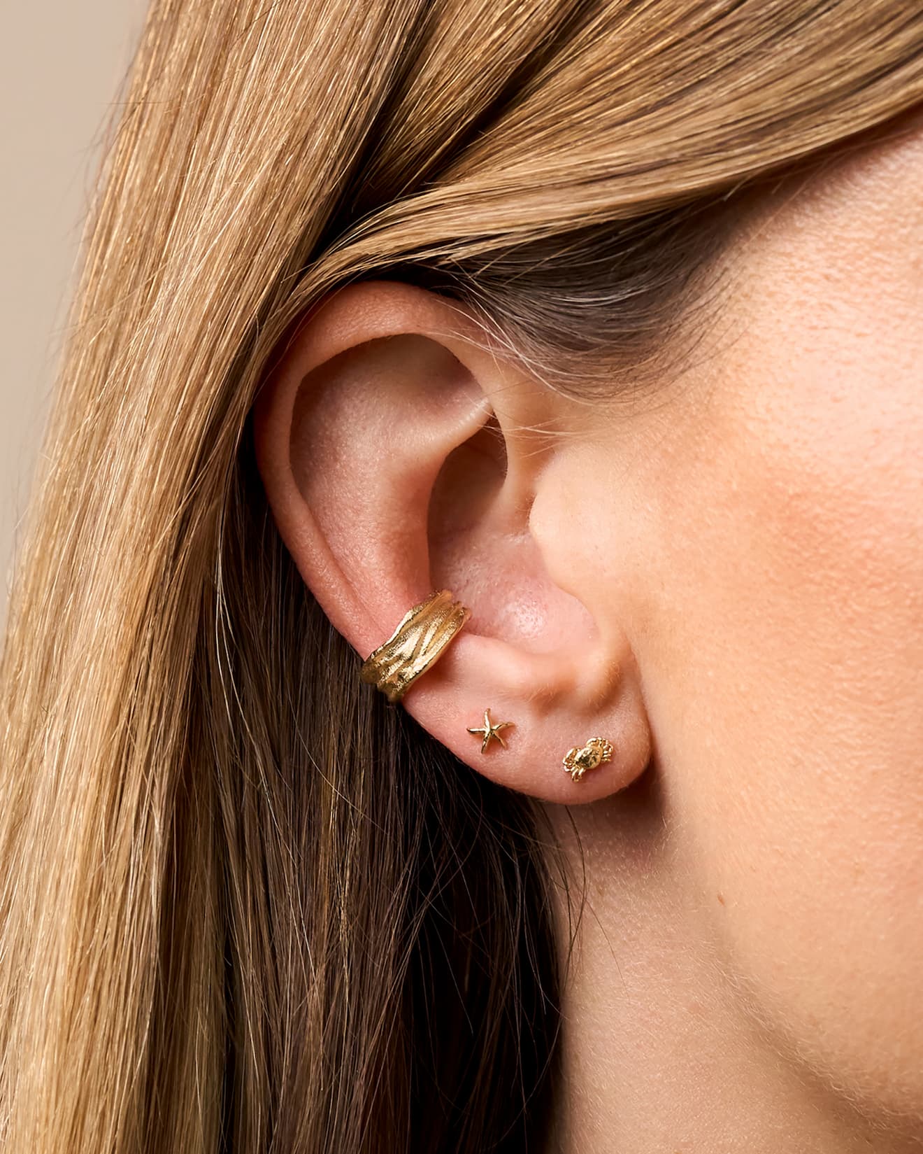 Ear styled with a textured gold ear cuff and starfish and crab piercing studs