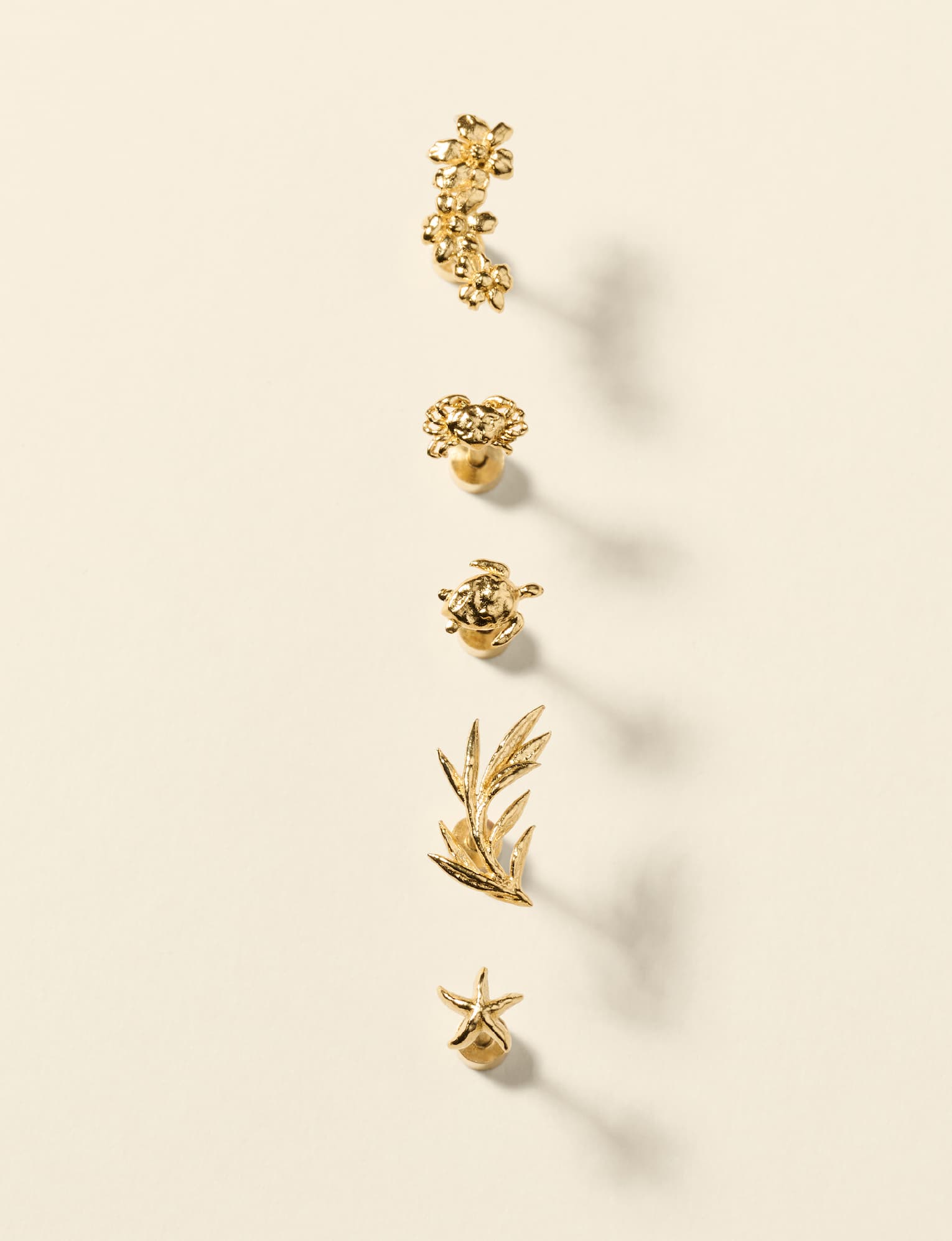 Gold piercing studs from the Ornata Collection: a climbing flower cluster, a flower, a sea turtle, an olive branch and a starfish