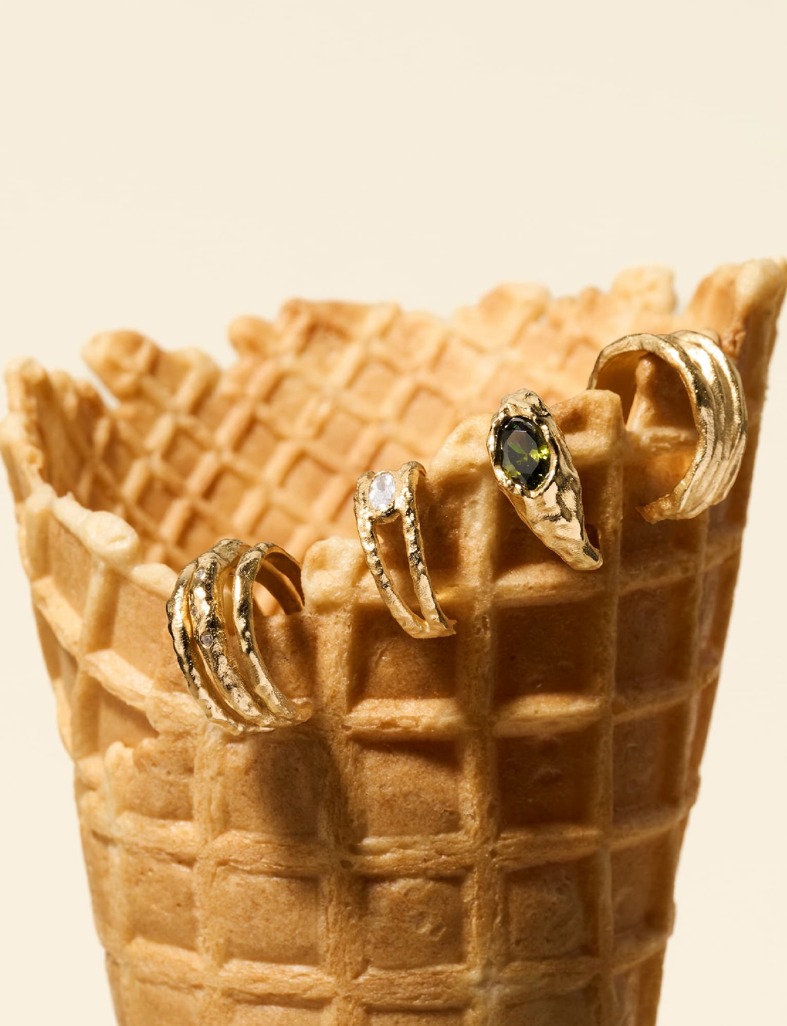 Three gold Ornata ear cuffs balanced on a waffle ice-cream cone, one set with a green stone