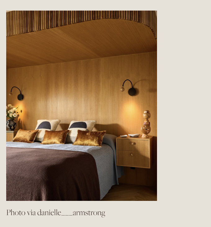 Wood paneled room with bed dressed in a plum and light blue blankets and golden pillows