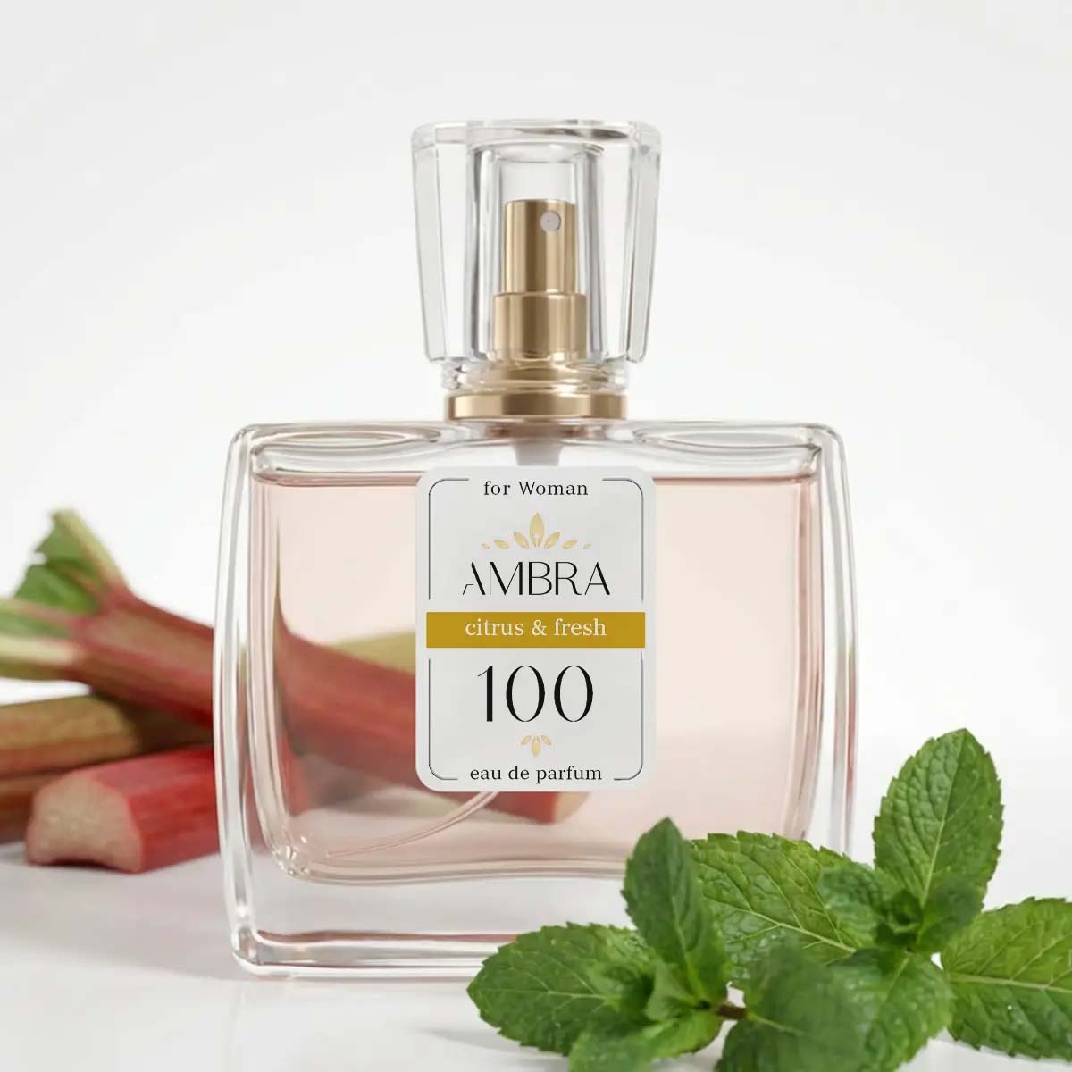 Glass perfume bottle labelled 'AMBRA citrus & fresh 100' eau de parfum for women, styled with rhubarb stalks and fresh mint leaves