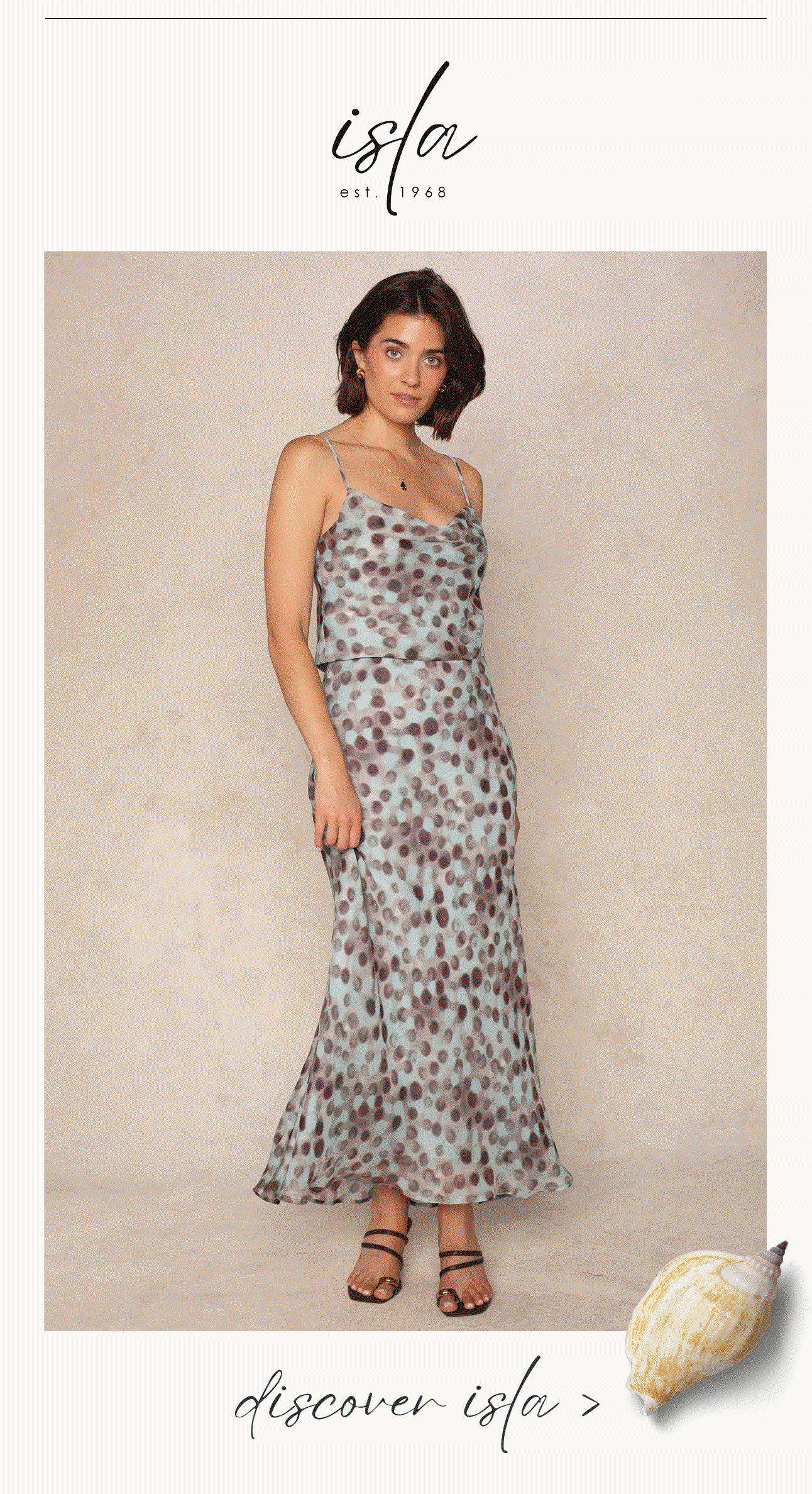 Model wearing a seafoam and plum spotted satin camisole with a matching maxi skirt, beneath the Isla est. 1968 logo and “Discover Isla” text.
