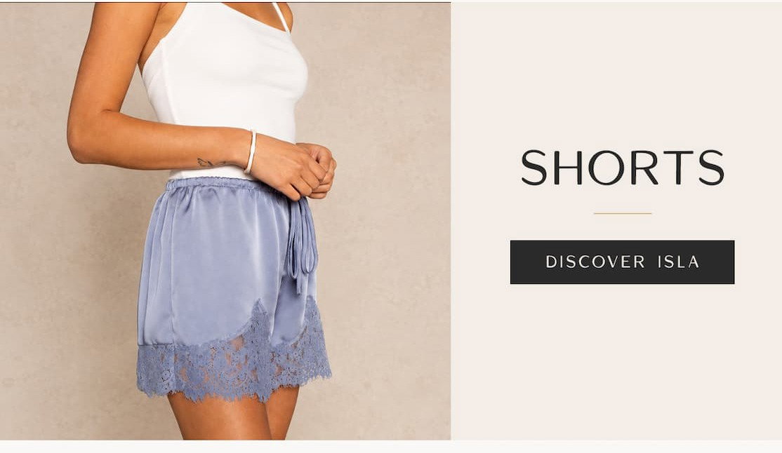 Model wearing a white tank top and light blue satin shorts with lace trim beside text reading “Shorts” and “Discover Isla.”