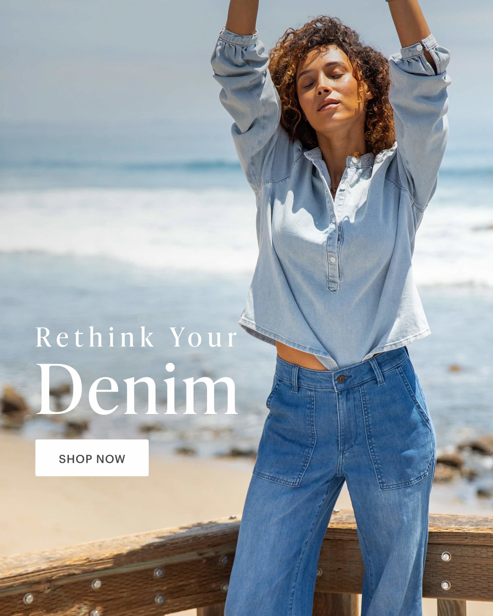 Rethink Your Denim - Woman in flowing light denim top and high waisted denim pants in relaxed pose by ocean. 