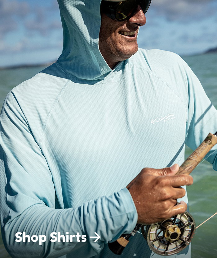 A man wearing a light blue sun hoodie on the water with text: Shop Tops