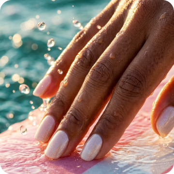 Close-up of a wet hand with Dashing Diva Pure Porcelain Glaze Effect resting on a pink surface, with water droplets and turquoise ocean in the background.